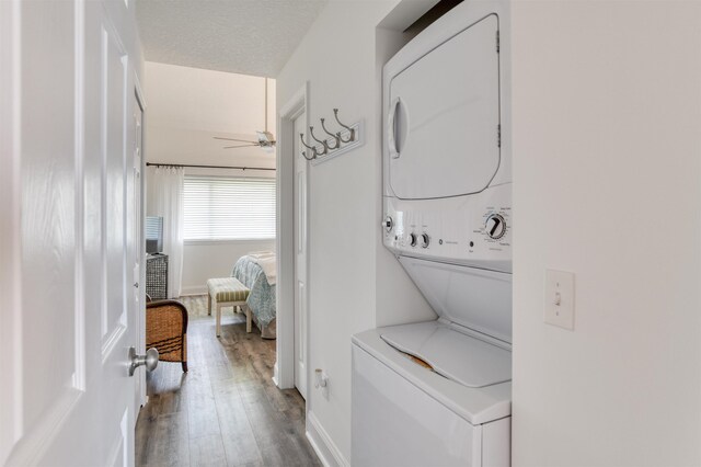 laundry area with stacked washer / dryer, ceiling fan, wood-type flooring, and a textured ceiling