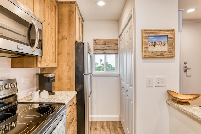 kitchen with backsplash, light hardwood / wood-style floors, light stone counters, and stainless steel appliances