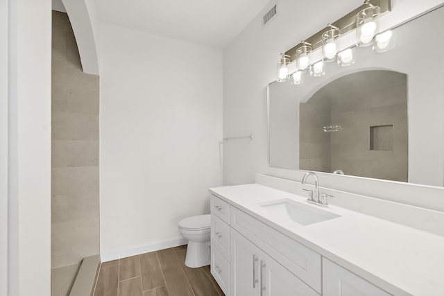 bathroom featuring tiled shower, vanity, and toilet