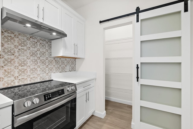 kitchen featuring white cabinets, light wood-type flooring, a barn door, and stainless steel range with electric stovetop