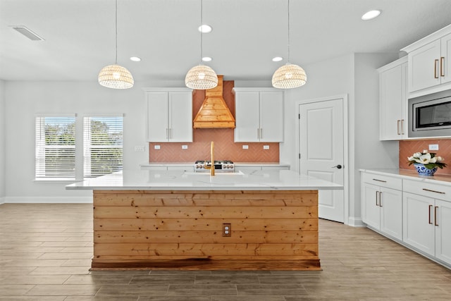 kitchen with light wood finished floors, visible vents, stainless steel microwave, custom exhaust hood, and white cabinetry