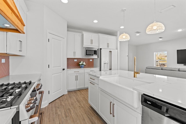 kitchen with premium appliances, hanging light fixtures, backsplash, white cabinets, and a sink