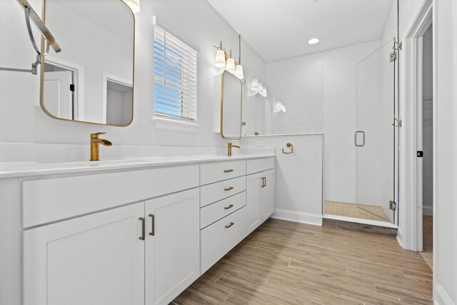 full bathroom featuring wood finish floors, double vanity, recessed lighting, a sink, and a shower stall