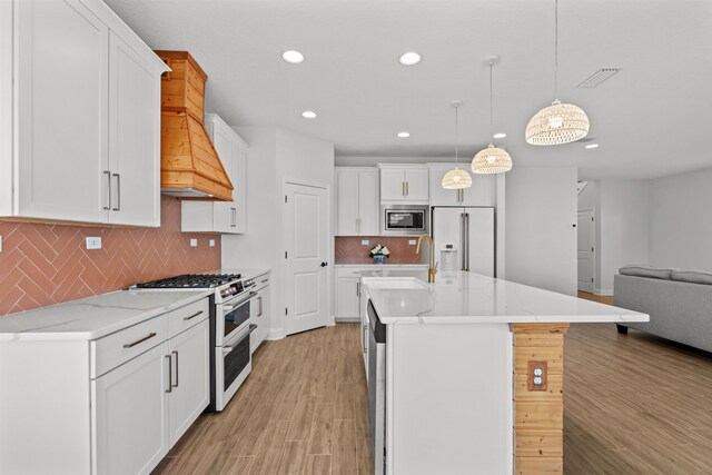 kitchen with light wood-style flooring, high quality appliances, open floor plan, white cabinetry, and a sink