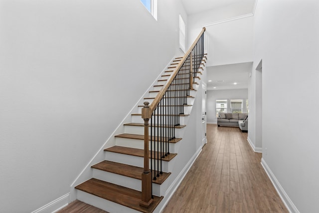 stairway featuring a high ceiling, wood finished floors, and baseboards