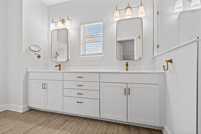 full bath featuring double vanity, baseboards, a tile shower, and wood finished floors