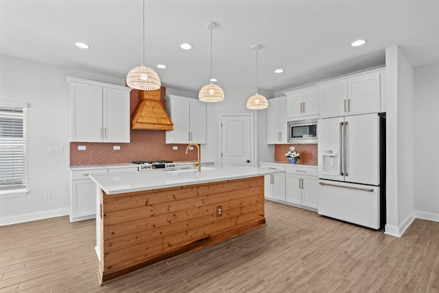 kitchen with high end white refrigerator, stainless steel microwave, custom exhaust hood, light countertops, and white cabinetry