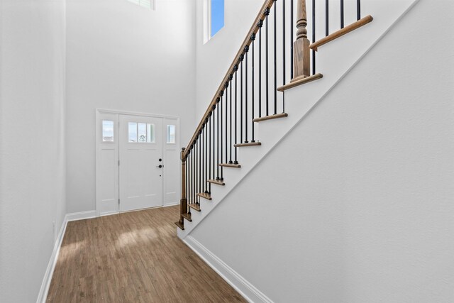 entryway featuring a high ceiling, stairway, baseboards, and wood finished floors