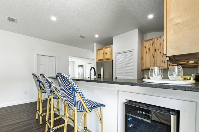 kitchen with stainless steel fridge, a textured ceiling, light brown cabinetry, dark hardwood / wood-style flooring, and beverage cooler