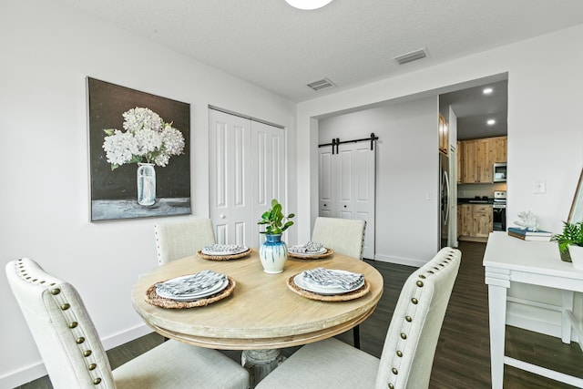 dining space featuring a barn door, wood-type flooring, and a textured ceiling