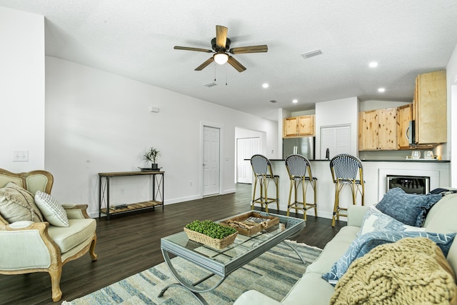 living room featuring ceiling fan, dark wood-type flooring, and a textured ceiling