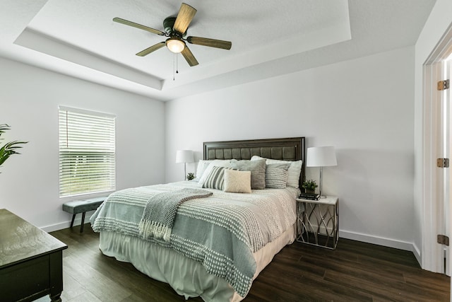 bedroom with ceiling fan, dark hardwood / wood-style flooring, and a tray ceiling