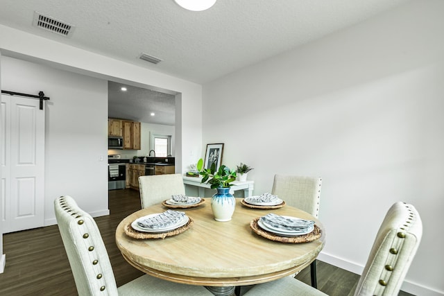 dining space with a textured ceiling, a barn door, and dark hardwood / wood-style flooring