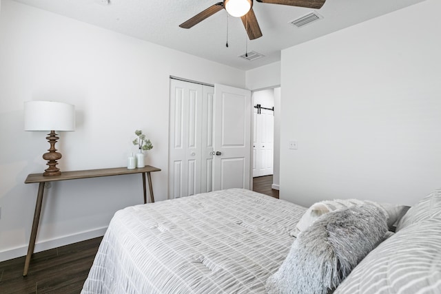 bedroom featuring ceiling fan, a barn door, dark wood-type flooring, and a closet