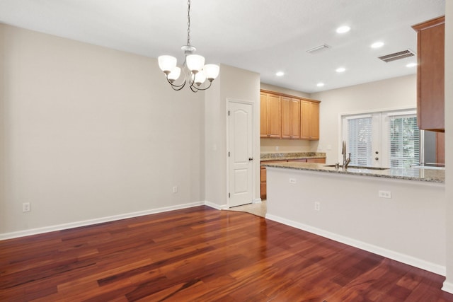 kitchen with light stone countertops, sink, dark wood-type flooring, an inviting chandelier, and kitchen peninsula