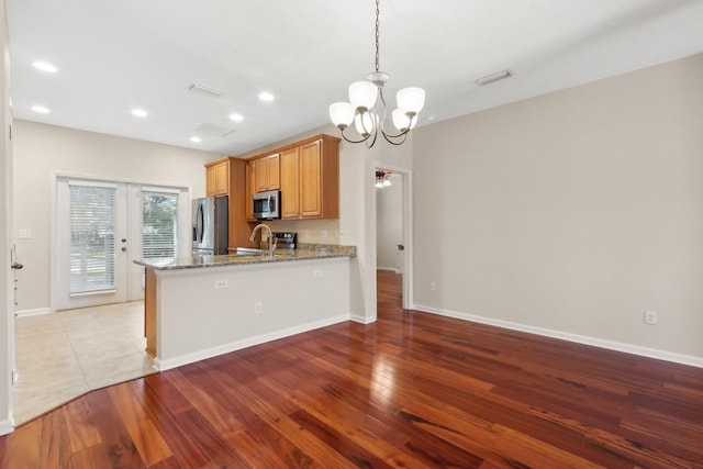 kitchen featuring kitchen peninsula, appliances with stainless steel finishes, light stone counters, pendant lighting, and light hardwood / wood-style flooring