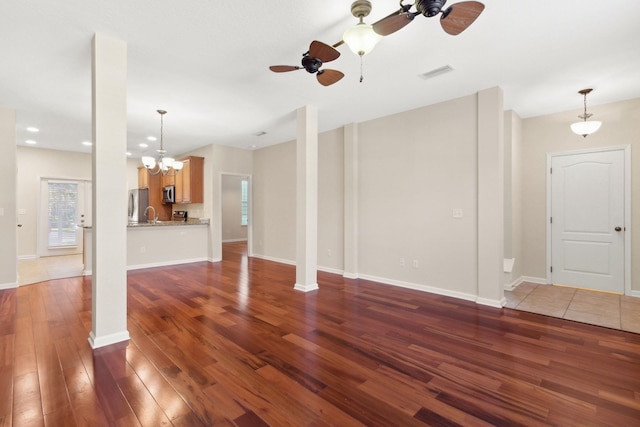 unfurnished living room featuring ceiling fan with notable chandelier and dark hardwood / wood-style floors