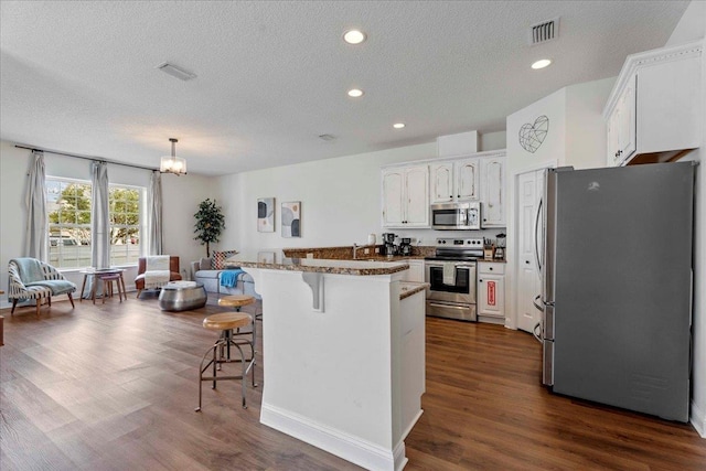 28 S Comares Ave, Saint Augustine, FL 32080 - kitchen featuring stainless steel appliances, a kitchen bar, a textured ceiling, dark wood-type flooring, and white cabinets
