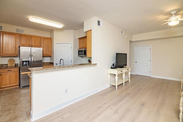 kitchen with sink, appliances with stainless steel finishes, kitchen peninsula, light stone countertops, and light hardwood / wood-style floors