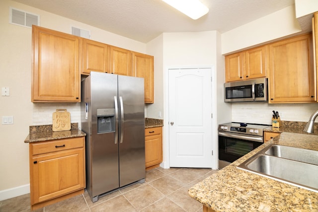 kitchen with sink, backsplash, light tile patterned flooring, and appliances with stainless steel finishes