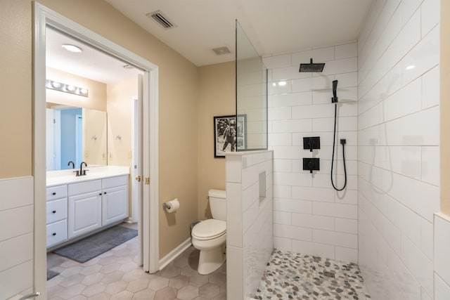 bathroom featuring tile patterned flooring, vanity, toilet, and tiled shower