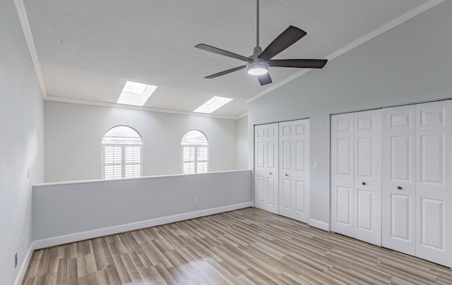 unfurnished bedroom with lofted ceiling with skylight, ceiling fan, ornamental molding, and light hardwood / wood-style flooring