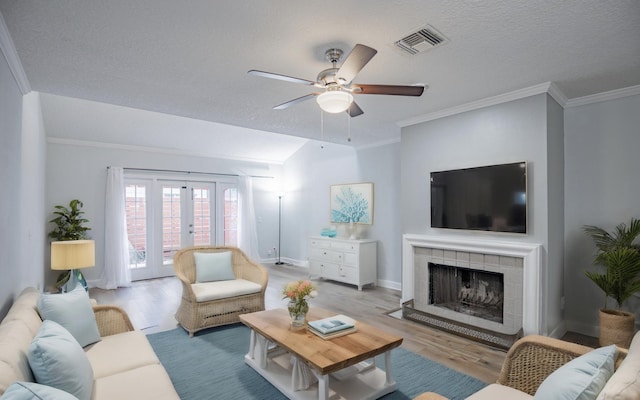 living room featuring a fireplace, light hardwood / wood-style floors, crown molding, and french doors