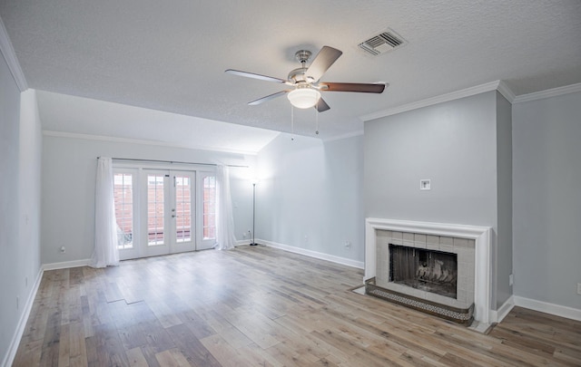 unfurnished living room featuring french doors, ceiling fan, ornamental molding, light hardwood / wood-style floors, and a tiled fireplace