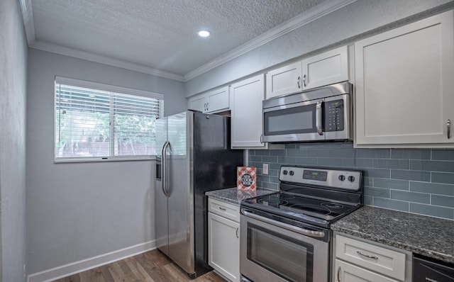 kitchen with dark stone counters, stainless steel appliances, crown molding, white cabinets, and dark hardwood / wood-style floors