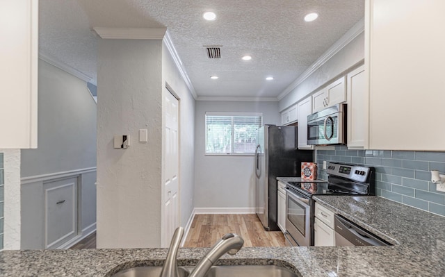 kitchen with dark stone countertops, white cabinetry, crown molding, and appliances with stainless steel finishes