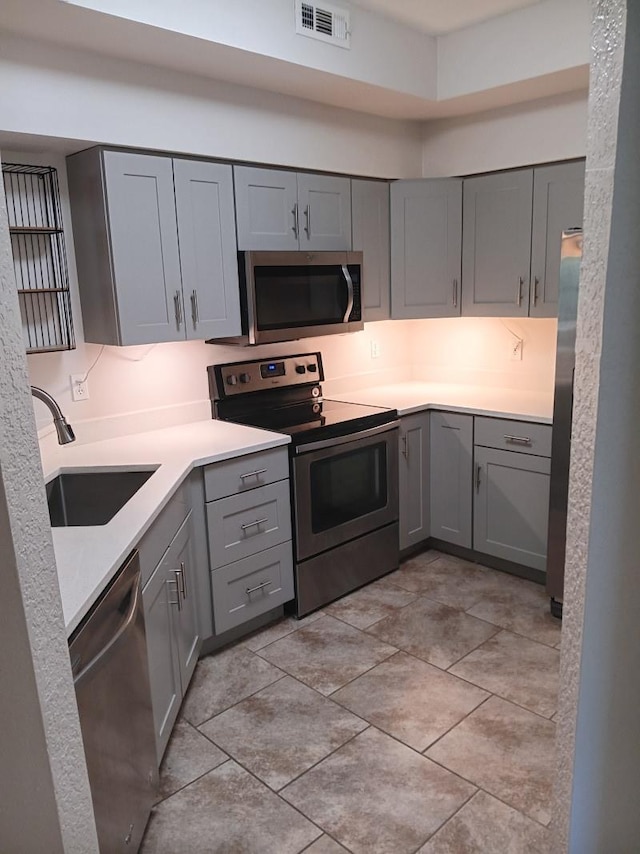 kitchen featuring visible vents, gray cabinetry, a sink, appliances with stainless steel finishes, and light countertops