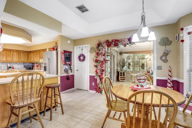 tiled dining space with a raised ceiling and an inviting chandelier