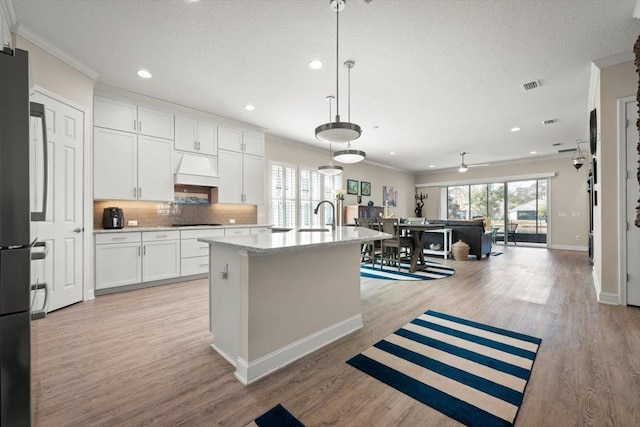 kitchen with crown molding, stainless steel refrigerator, an island with sink, pendant lighting, and white cabinets