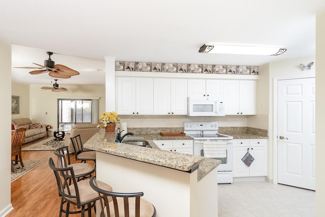 kitchen featuring kitchen peninsula, a kitchen breakfast bar, white appliances, white cabinets, and light hardwood / wood-style floors