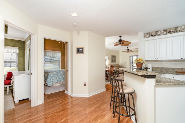 kitchen featuring kitchen peninsula, a textured ceiling, light hardwood / wood-style floors, white cabinetry, and a breakfast bar area