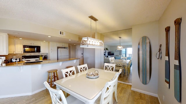 dining area featuring visible vents, light wood-style flooring, baseboards, and a textured ceiling