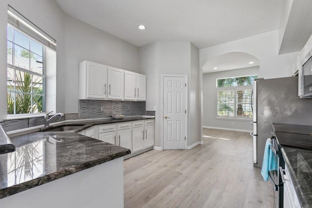 kitchen with sink, white cabinets, stainless steel electric stove, dark stone counters, and light wood-type flooring