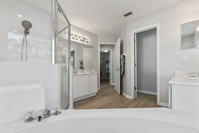 bathroom with plus walk in shower, hardwood / wood-style floors, vanity, and a textured ceiling