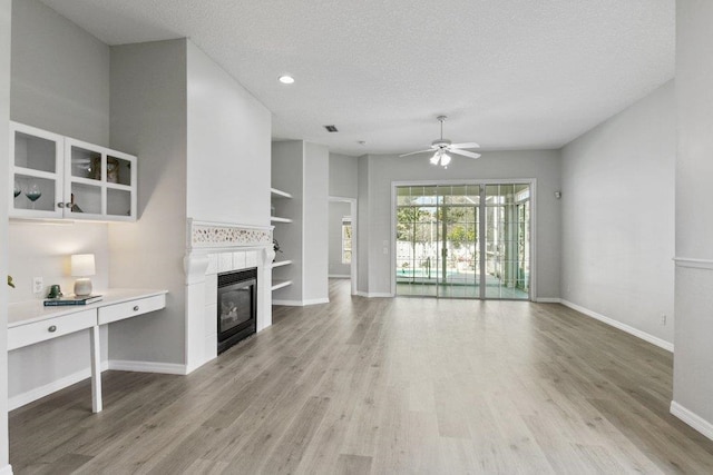 unfurnished living room featuring a tile fireplace, built in features, ceiling fan, and light hardwood / wood-style floors