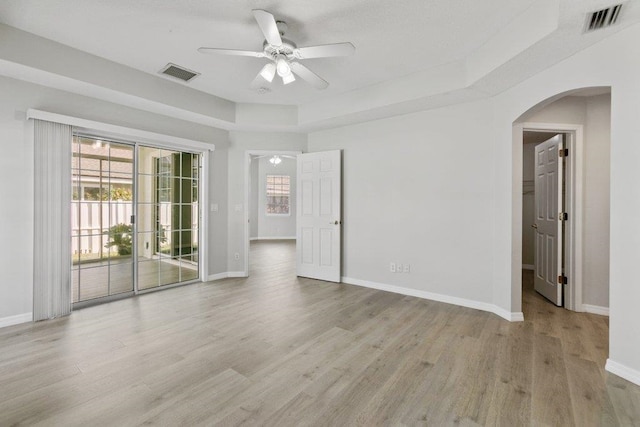 empty room featuring a tray ceiling, ceiling fan, and light wood-type flooring