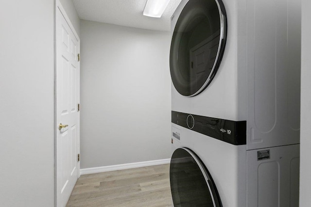 clothes washing area featuring stacked washing maching and dryer and light hardwood / wood-style floors