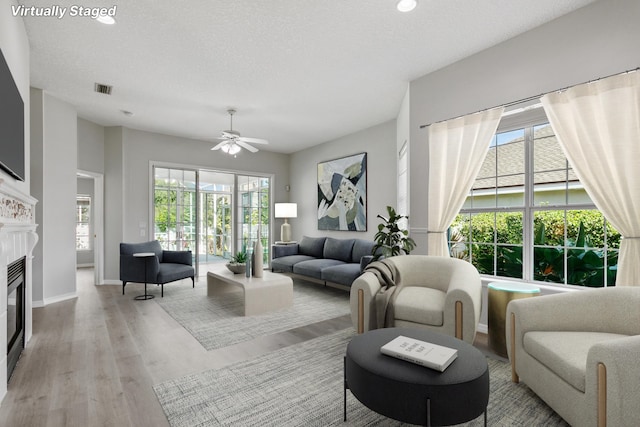 living room with ceiling fan, a textured ceiling, and light hardwood / wood-style flooring