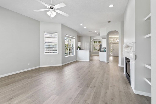 unfurnished living room featuring ceiling fan with notable chandelier and light hardwood / wood-style floors