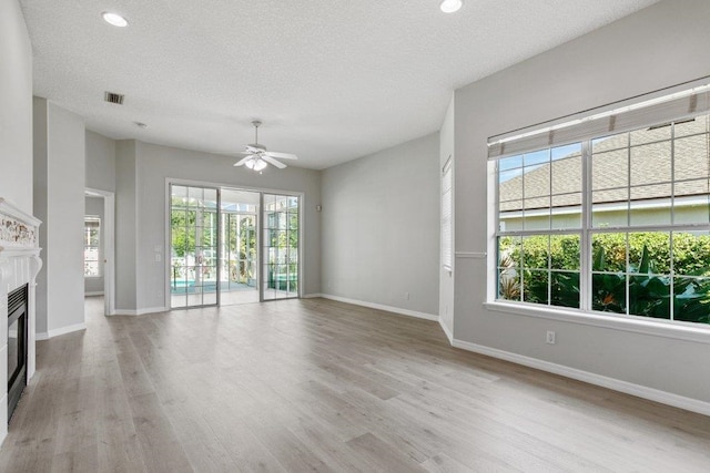 unfurnished living room featuring ceiling fan, a fireplace, light hardwood / wood-style floors, and a textured ceiling