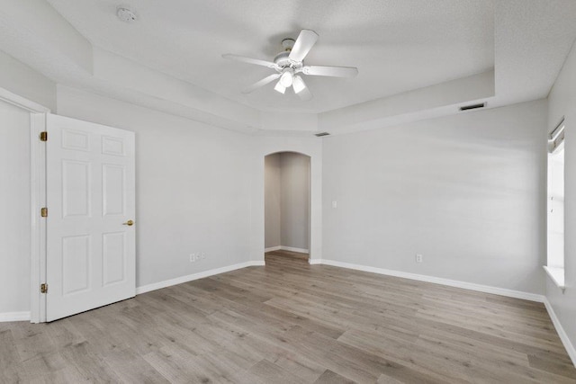 empty room featuring a raised ceiling, ceiling fan, and light wood-type flooring