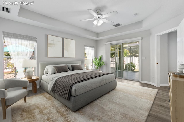 bedroom featuring hardwood / wood-style flooring, access to exterior, ceiling fan, and a tray ceiling