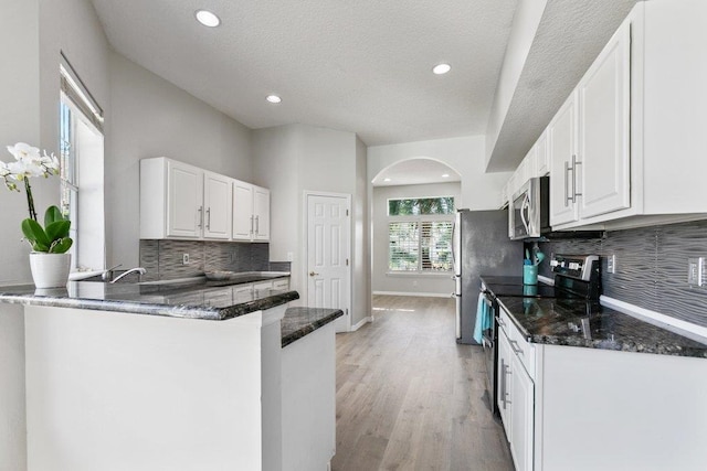 kitchen featuring white cabinetry, stainless steel appliances, kitchen peninsula, and dark stone counters