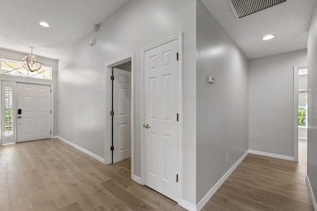 foyer featuring a notable chandelier, a textured ceiling, and light wood-type flooring