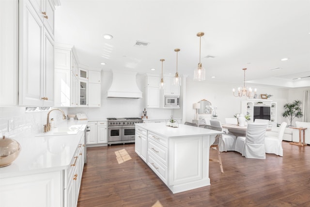 kitchen featuring custom range hood, a kitchen island, decorative light fixtures, double oven range, and white cabinetry