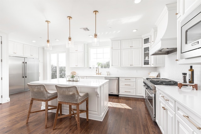 kitchen featuring built in appliances, a center island, white cabinets, and hanging light fixtures